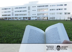 Vista de la fachada de la Facultad de Psicología de la UNLP. Libro impreso en primer plano.